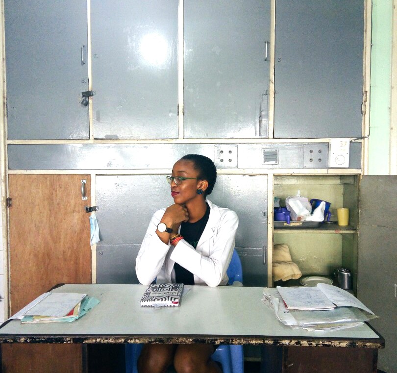 Housemanship In Nigeria (LUTH) Chronicles, Nigerian blogger Cassie Daves sitting at a desk in hospital holding cassie daves blog planner