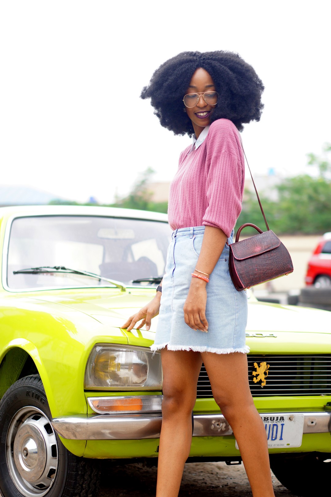 nigerian blogger Cassie daves wearing a denim mini skirt, mauve sweat shirt. leaning against a lemon green peugeot 504