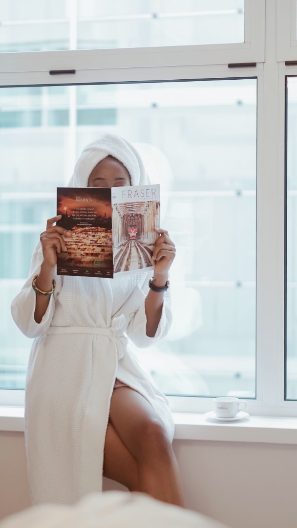 Cassie daves in a robe holding a magazine at fraser suites abuja