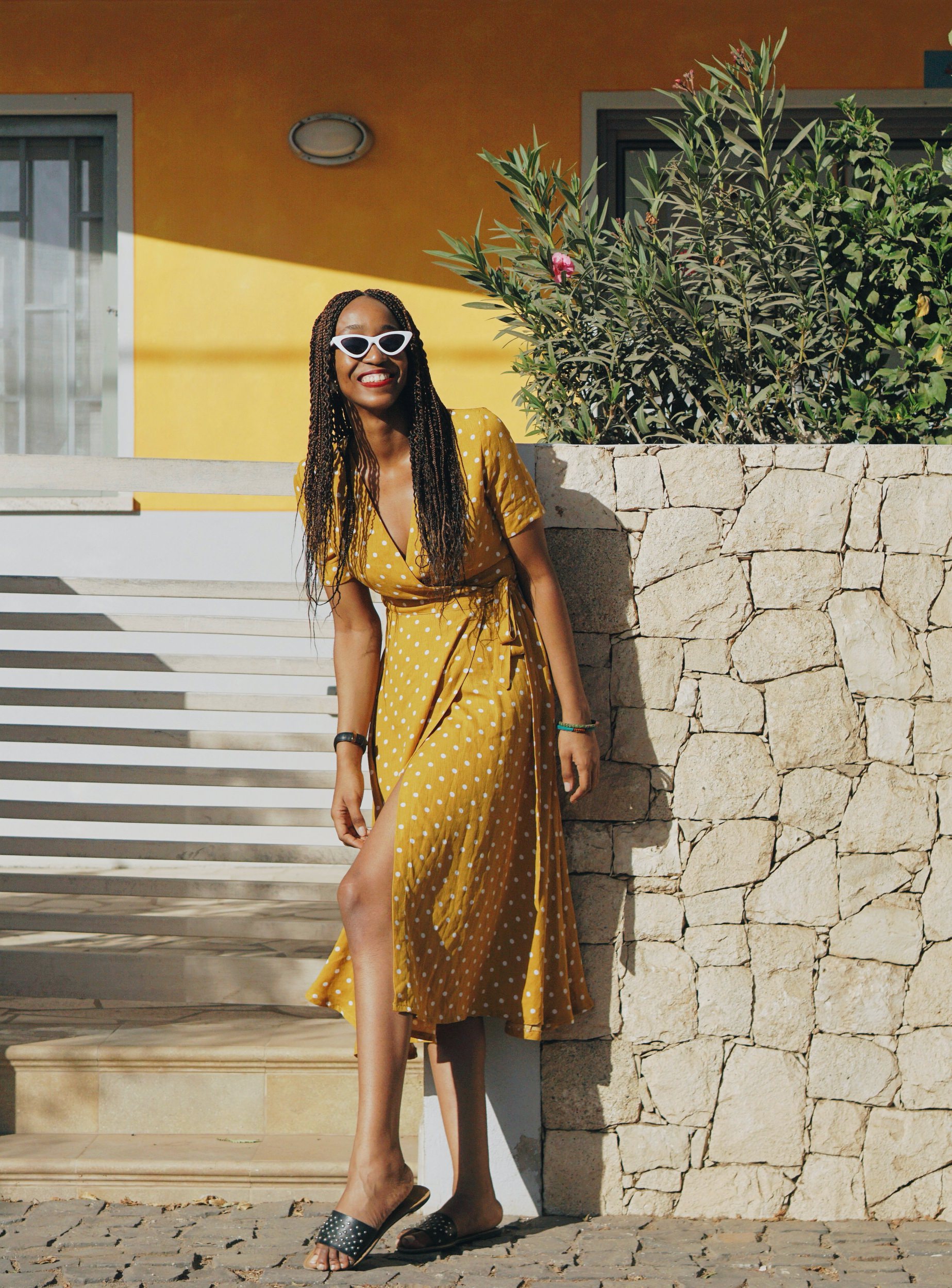 Cassie Daves wearing a yellow polka dot dress posing in front of a yellow house 