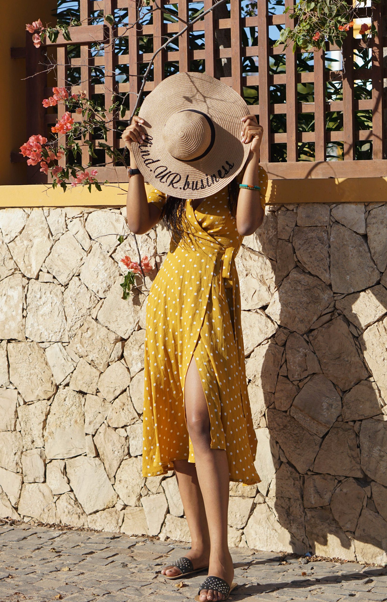 Cassie Daves wearing a yellow polka dot dress and holding a straw hat