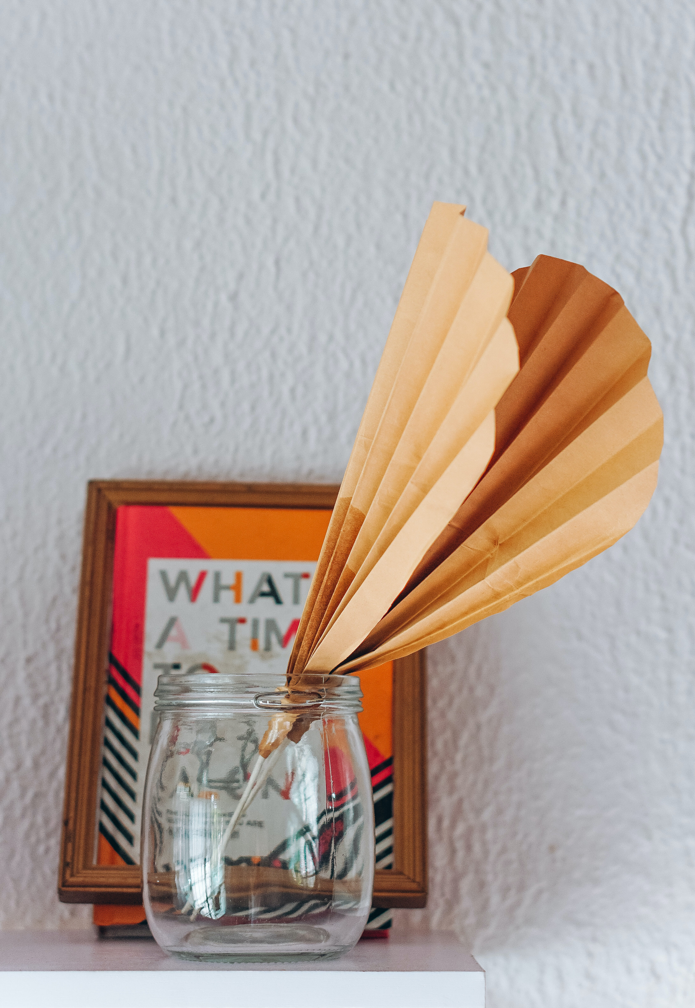 mason jar and a faux diy paper palm frond on a home office shelf 