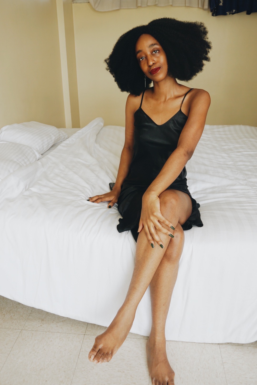 Cassie Daves sitting on a bed wearing a black slip dress